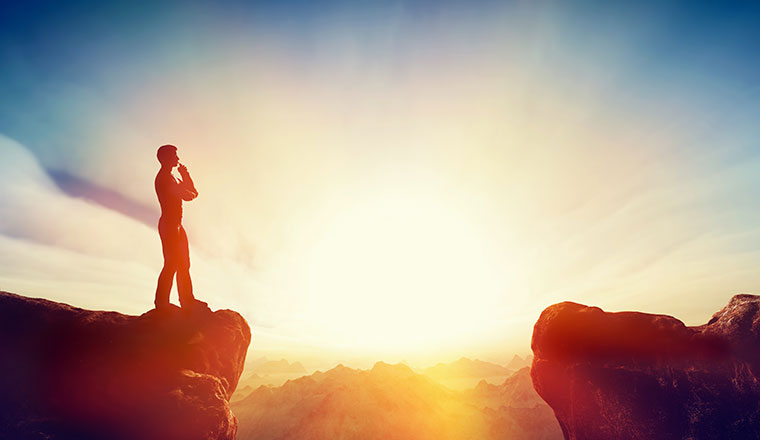 A person standing on a cliff looking at sunset