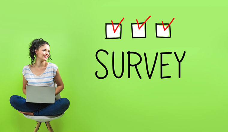 A woman sat on a chair on a laptop,looks at the word survey with boxes ticked