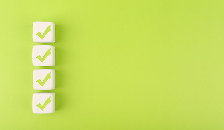 Four checkmarks on white cubes against bright green background - testing results concept