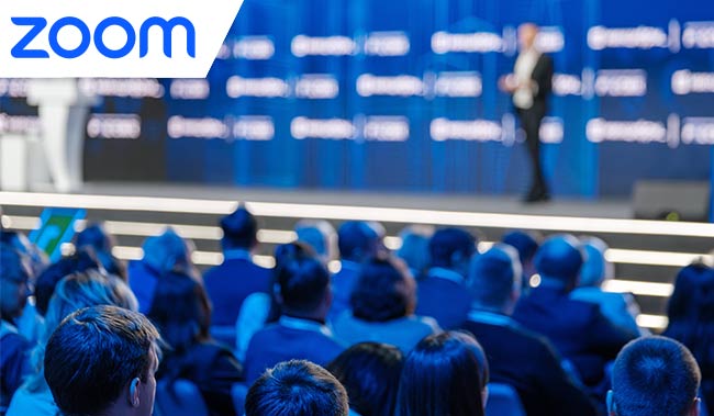 Audience attentively listening to keynote speaker at a corporate event with blurred conference background.