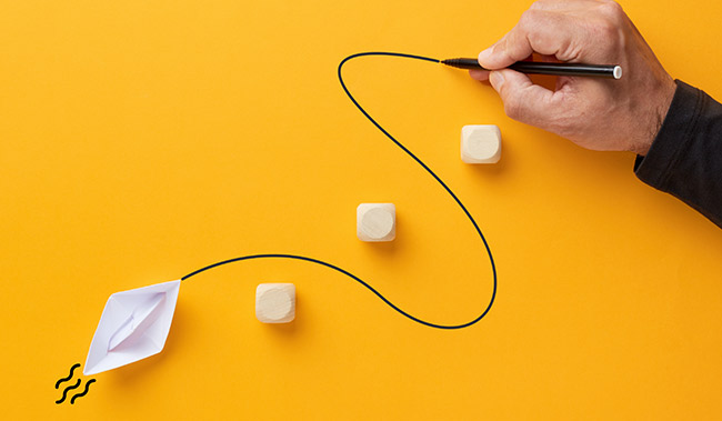 Male hand draws a curved line that guides a paper boat to cross the barriers.