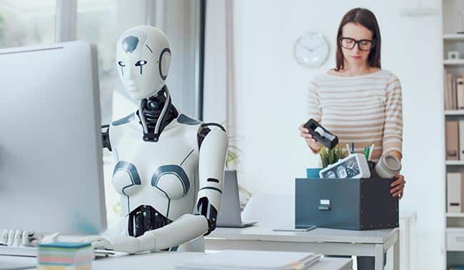 Disappointed businesswoman packing her belongings and leaving the office with an AI robot sat at the desk on the computer