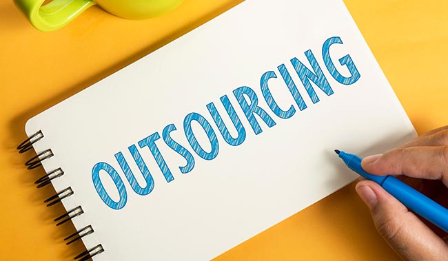 A notepad with the word outsourcing on it on a yellow background