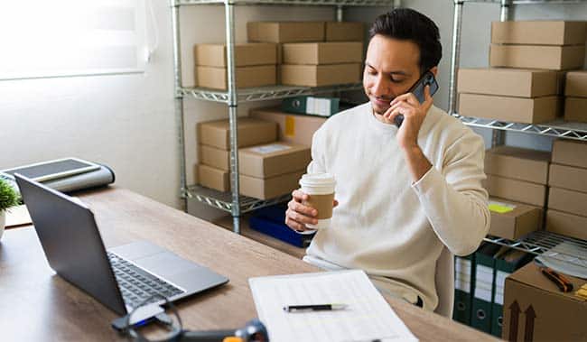 Entrepreneur multitasking in his small business warehouse: sipping coffee, chatting on the phone, and managing orders