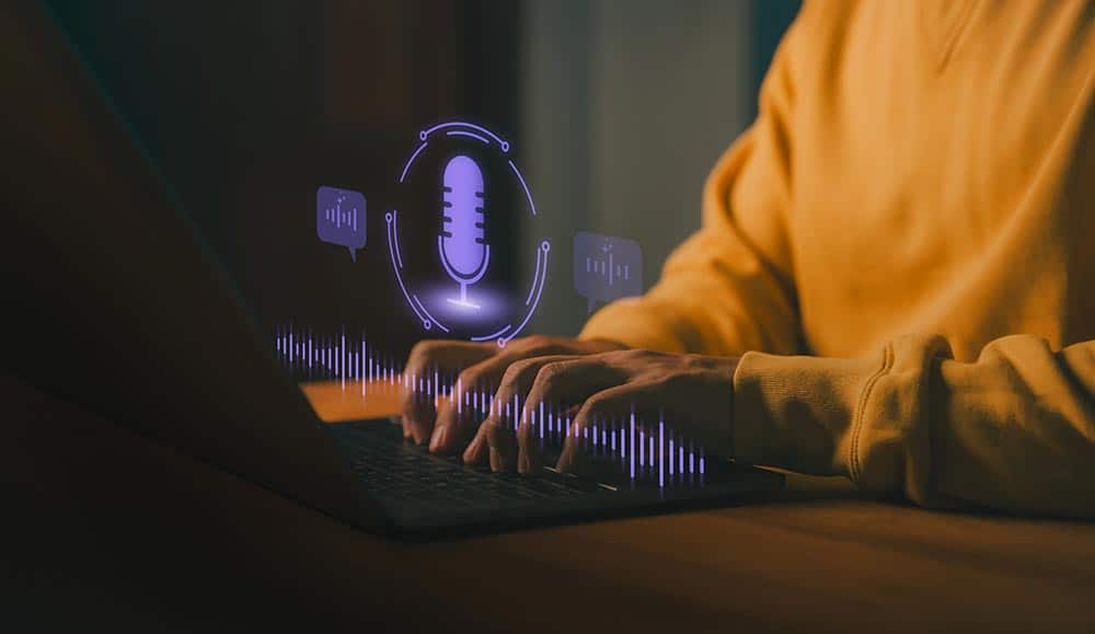 Person typing on laptop computer with glowing microphone and soundwave icon, representing speech recognition