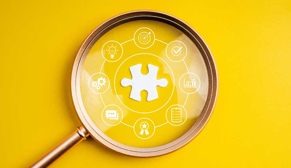 Magnifying glass focusing on puzzle piece with business strategy icons, representing elements of employee experience