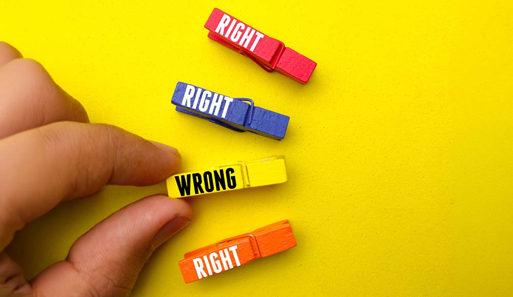Hand holding colored wooden clips with word RIGHT and WRONG on a yellow background.