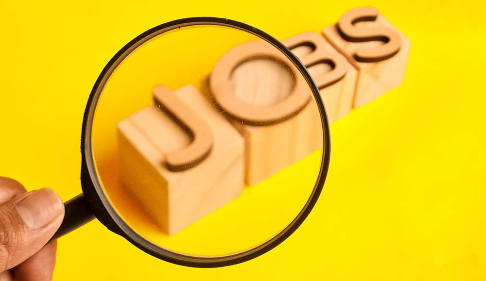 Magnifying glass highlighting the word jobs on wooden blocks representing career and job roles